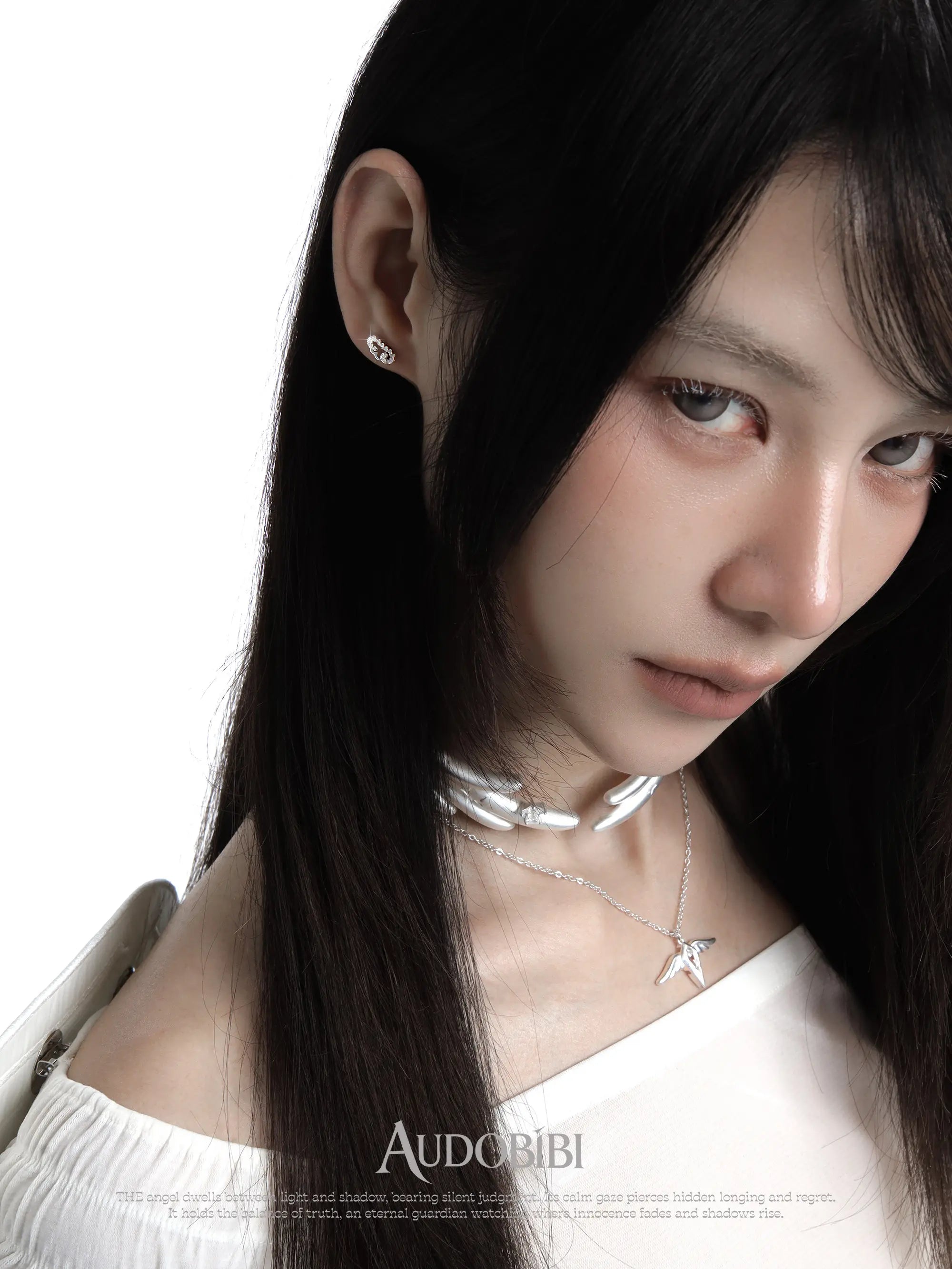 Angel-wing studs and cross hoop earrings, worn with other jewelry in a model portrait.