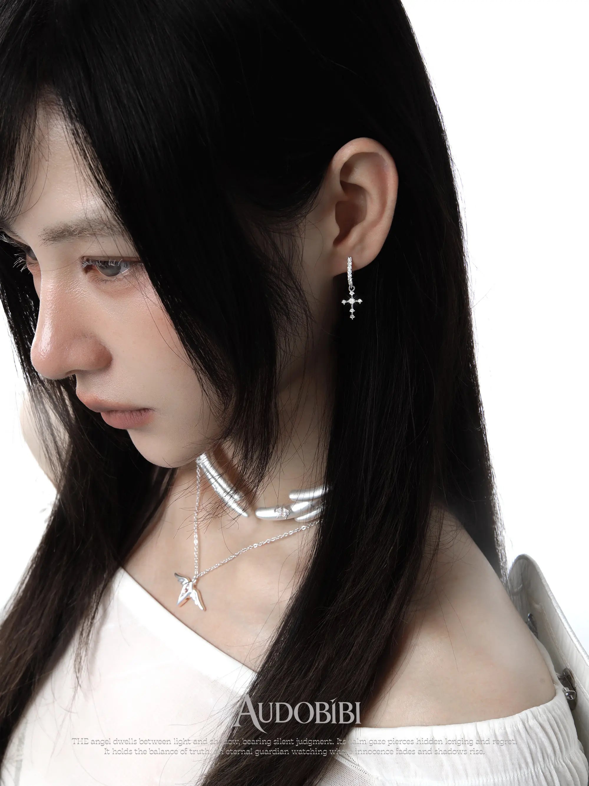 Angel-wing studs and cross hoop earrings, worn with other jewelry in a model portrait.
