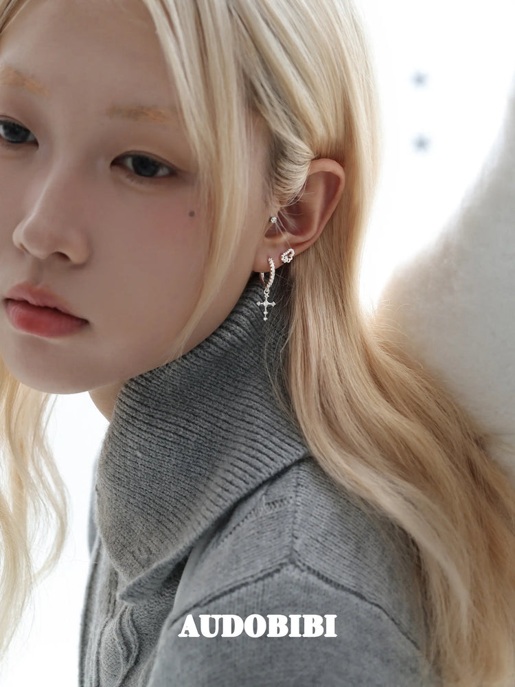 Angel-wing studs and cross hoop earrings, worn with other jewelry in a model portrait.