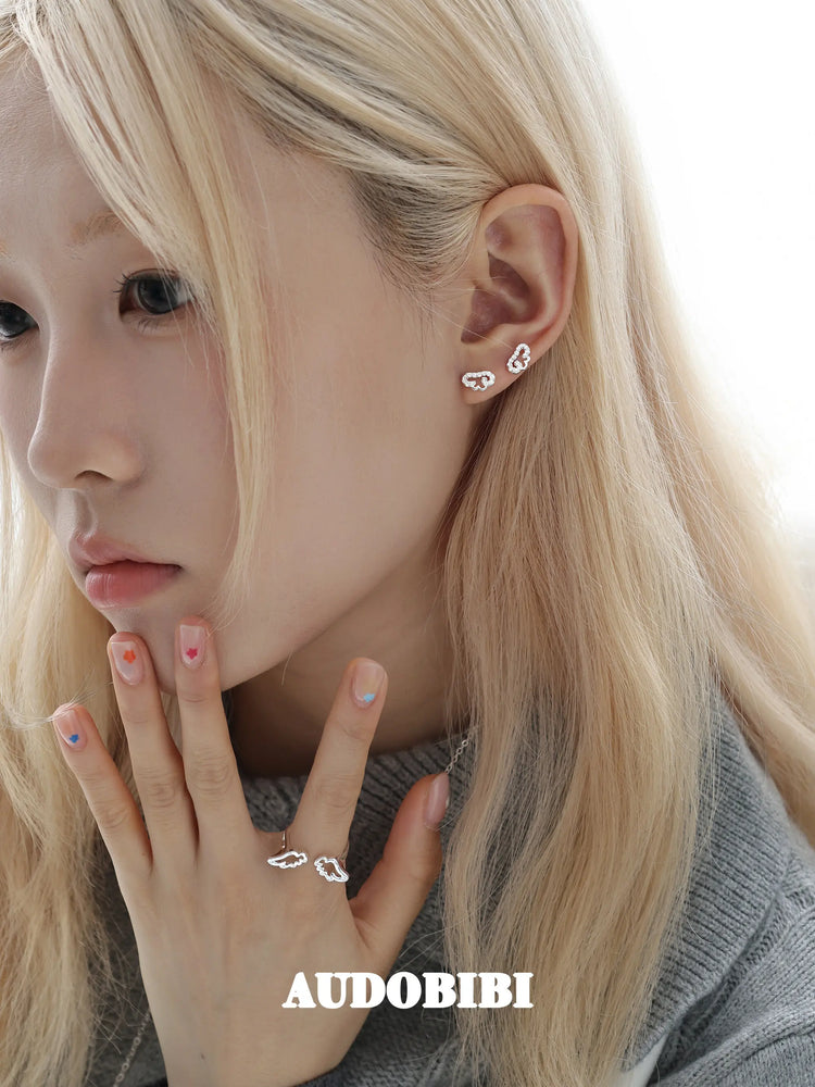 Angel-wing studs and cross hoop earrings, worn with other jewelry in a model portrait.