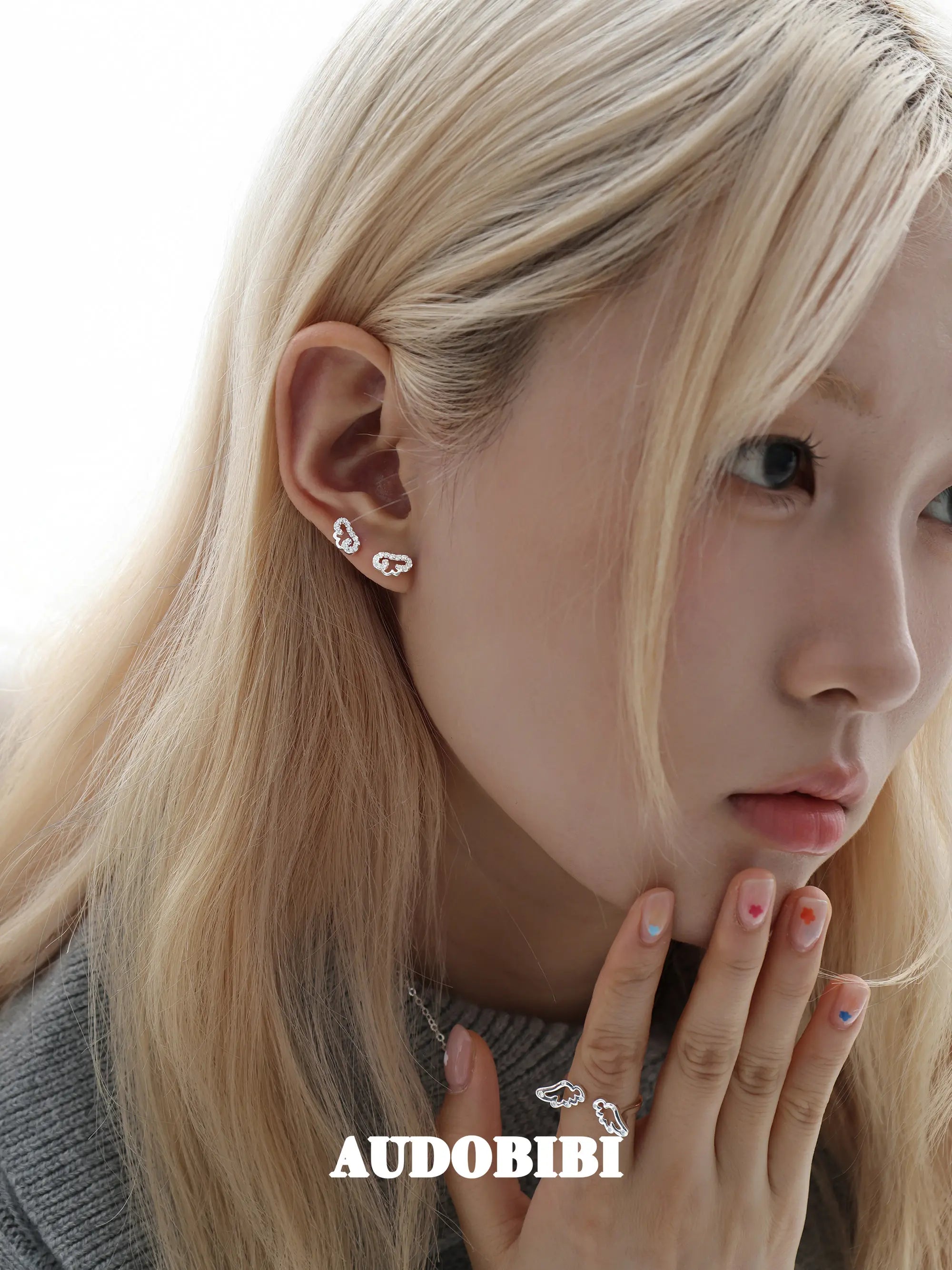 Angel-wing studs and cross hoop earrings, worn with other jewelry in a model portrait.