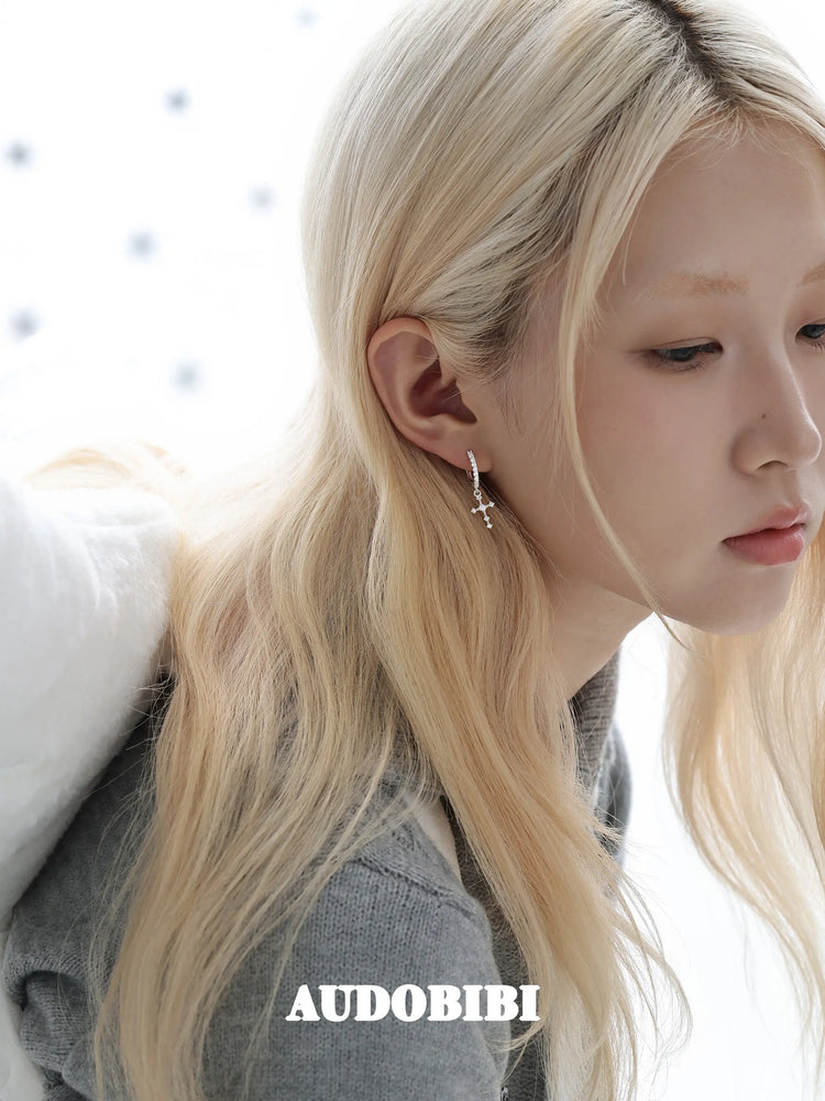 Angel-wing studs and cross hoop earrings, worn with other jewelry in a model portrait.