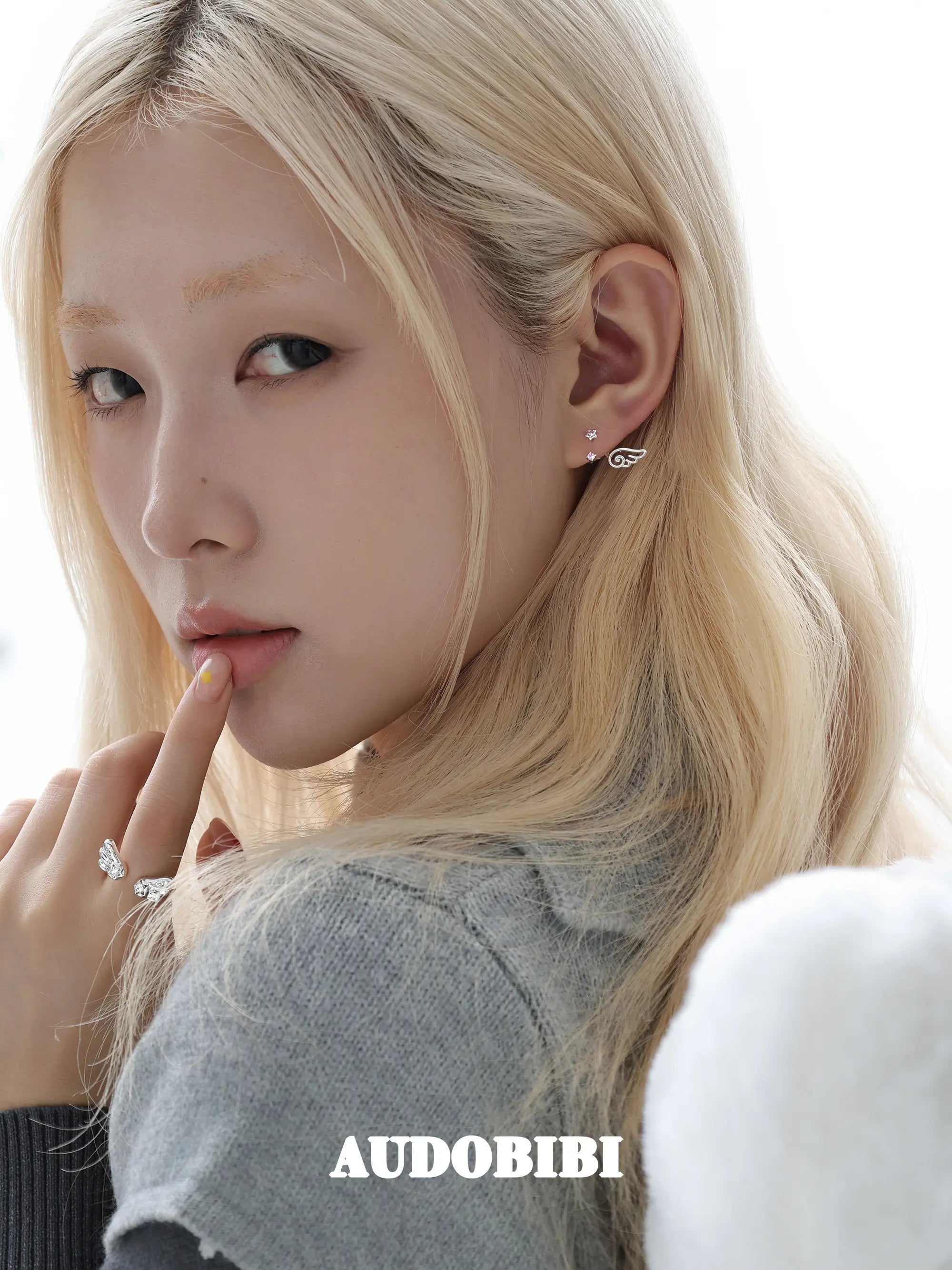 Open ring with rounded angel wings, worn with other jewelry in a model portrait.