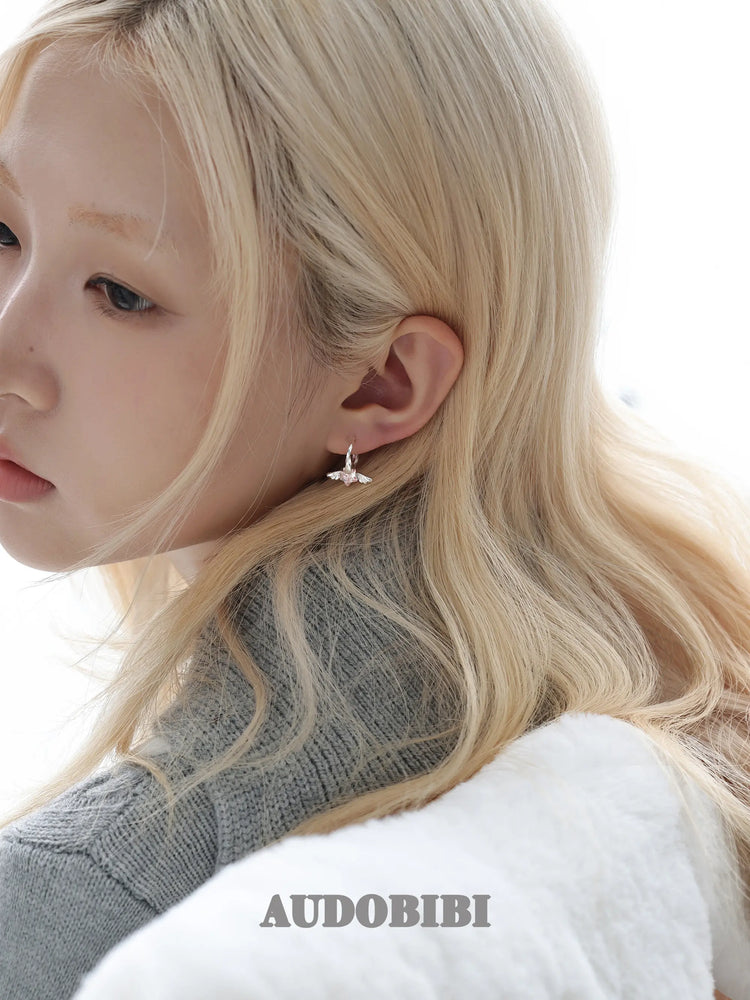 Mini wing-and-star hoop earrings, worn with other jewelry in a model portrait.