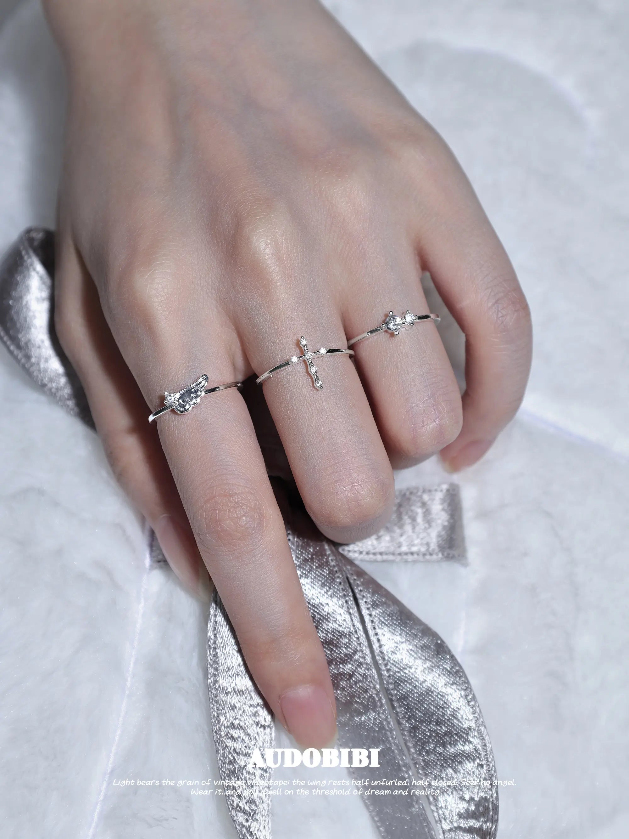 Cross and wing rings, shown on the hand or wrist with other jewelry.