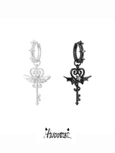 Silver-tone angel-key and black devil-key hoop earrings shown together.