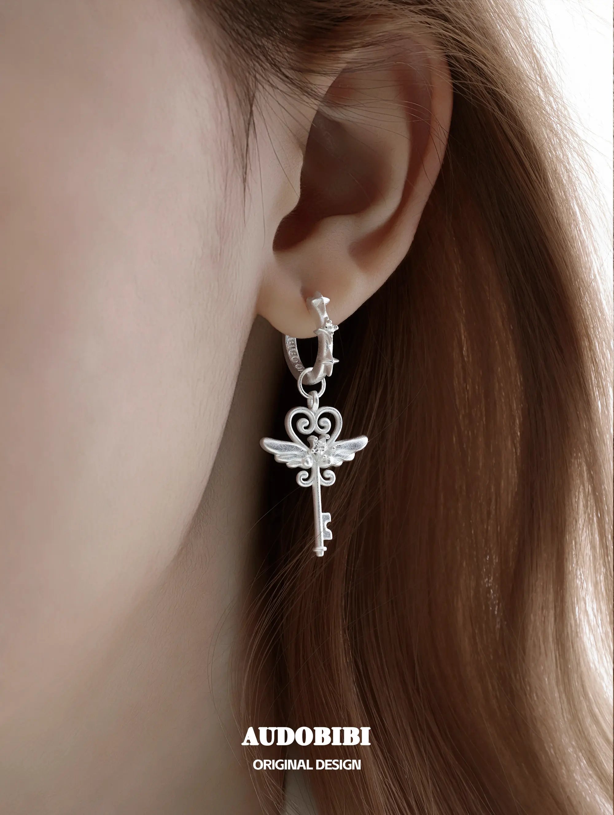 Winged-key hoop earrings, shown in a close-up of the ear.