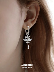 Winged-key hoop earrings, shown in a close-up of the ear.