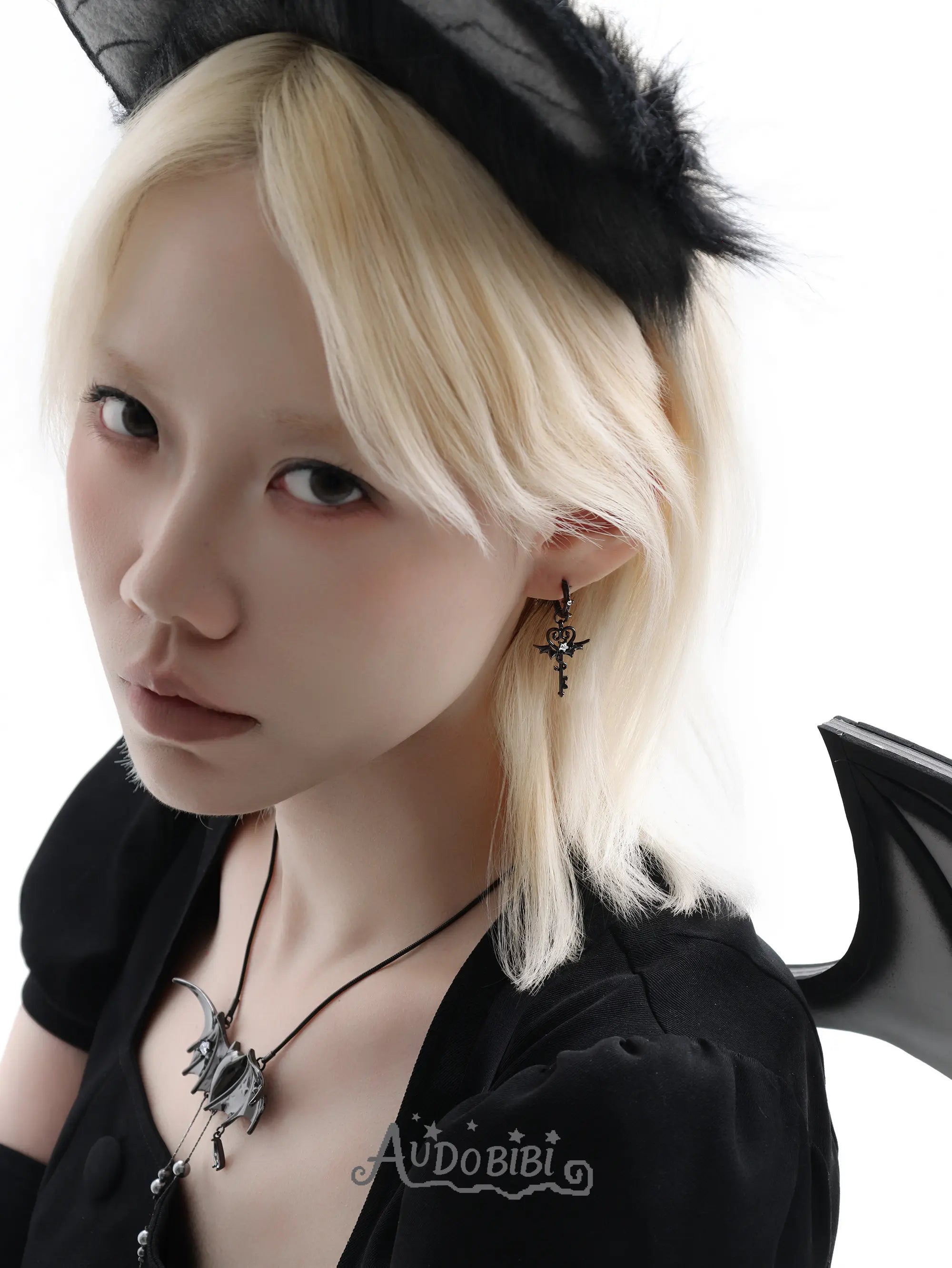 Black bat-wing pendant necklace, worn with other jewelry in a model portrait.