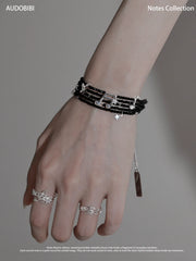 Black spinel musical-note bracelet, shown on the hand or wrist with other jewelry.