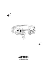 Musical-note ring with a wing detail and small round drop, viewed from the front.