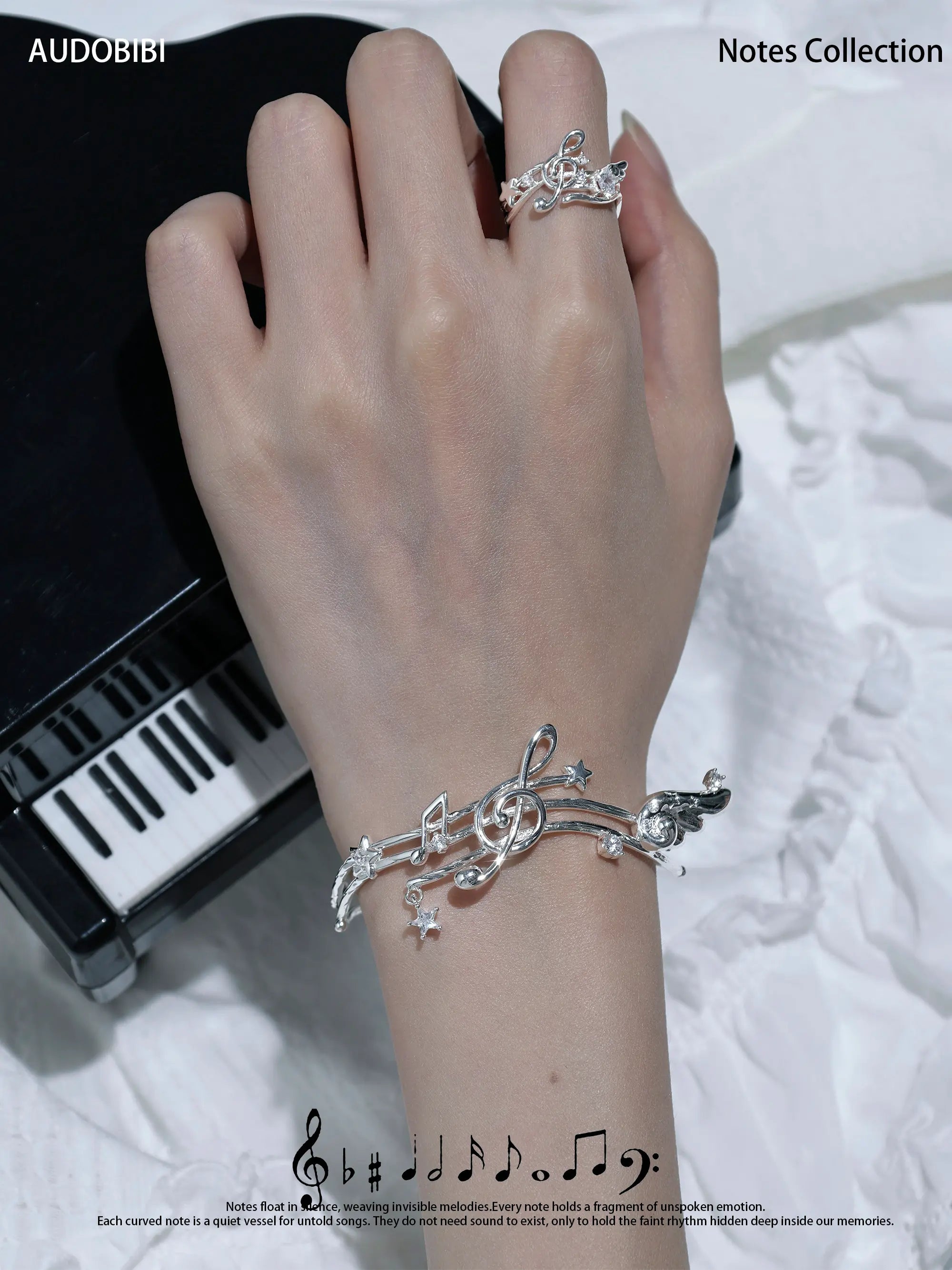 Musical-staff open bangle, shown on the hand or wrist with other jewelry.