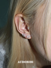 Angel-wing studs and cross hoop earrings, shown in a close-up of the ear.