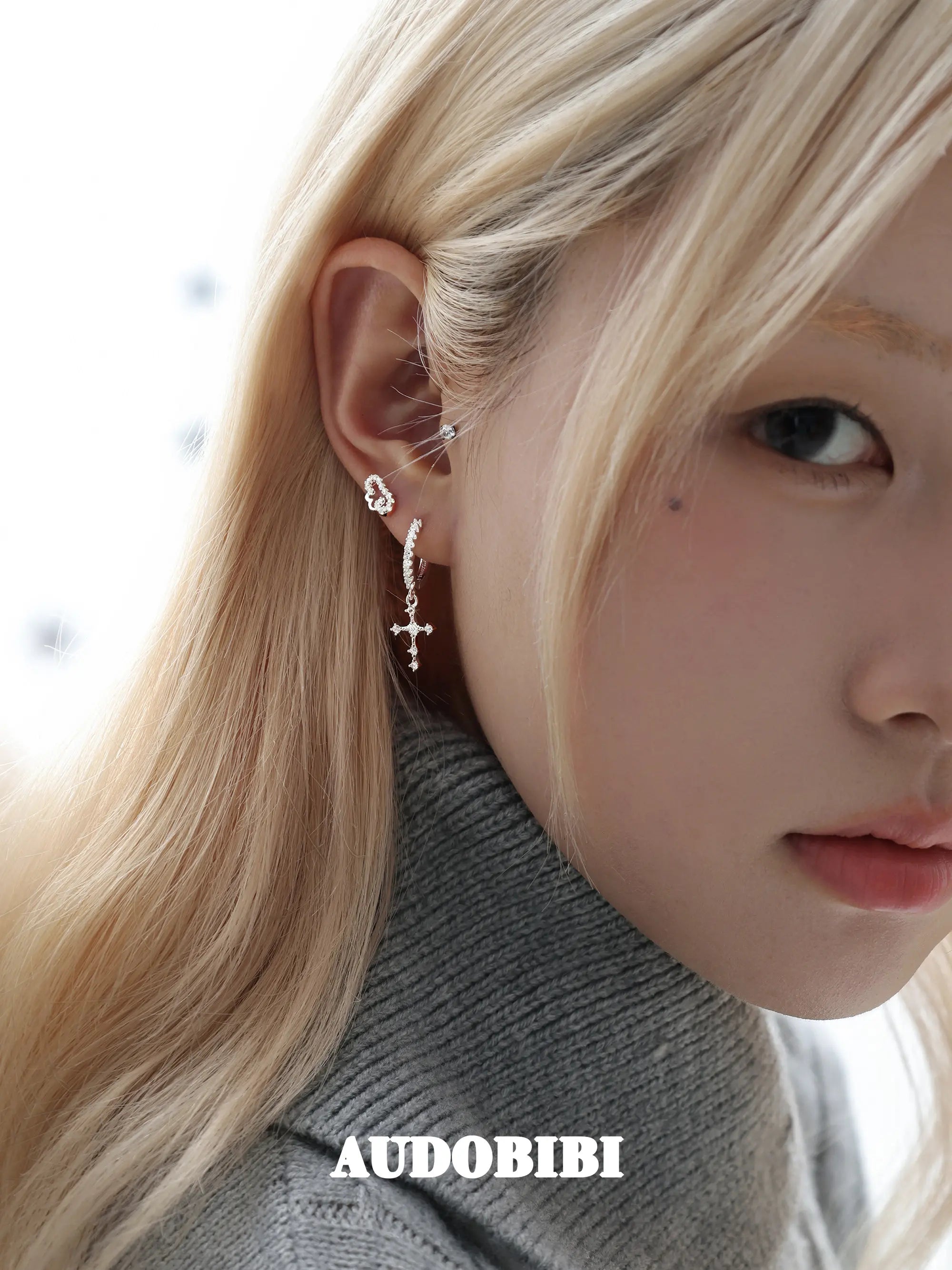 Angel-wing studs and cross hoop earrings, worn with other jewelry in a model portrait.
