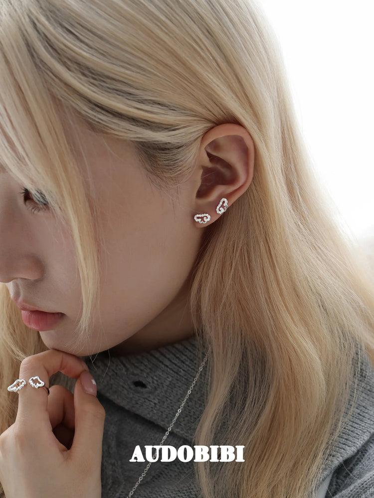 Angel-wing studs and cross hoop earrings, worn with other jewelry in a model portrait.