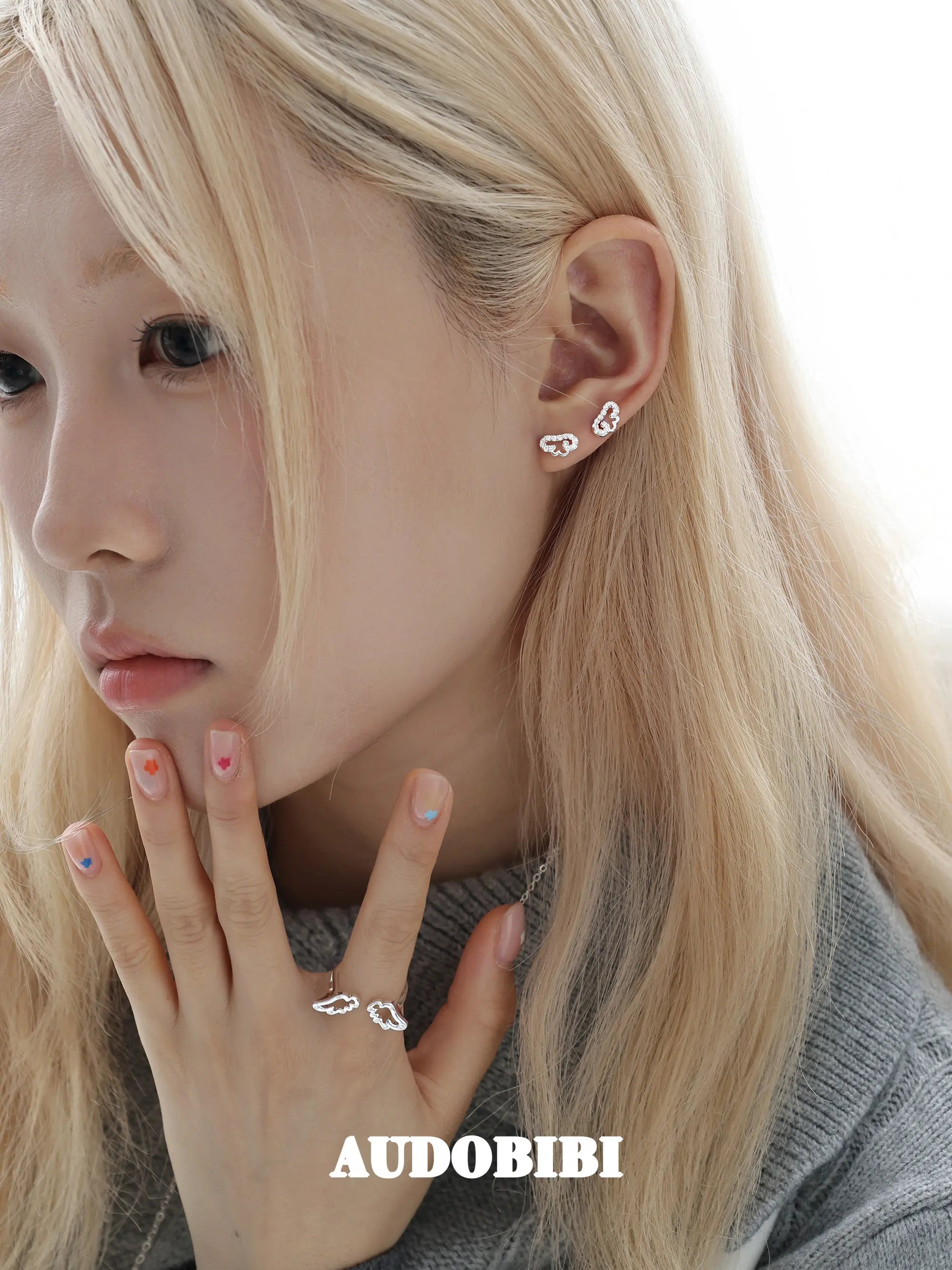 Angel-wing studs and cross hoop earrings, worn with other jewelry in a model portrait.