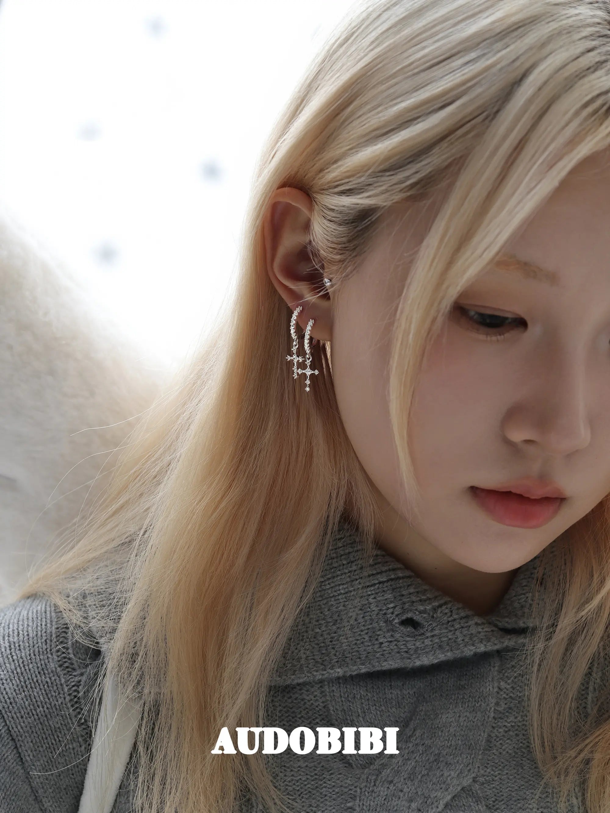 Angel-wing studs and cross hoop earrings, worn with other jewelry in a model portrait.