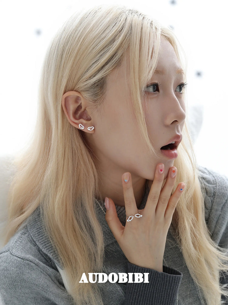 Angel-wing studs and cross hoop earrings, worn with other jewelry in a model portrait.
