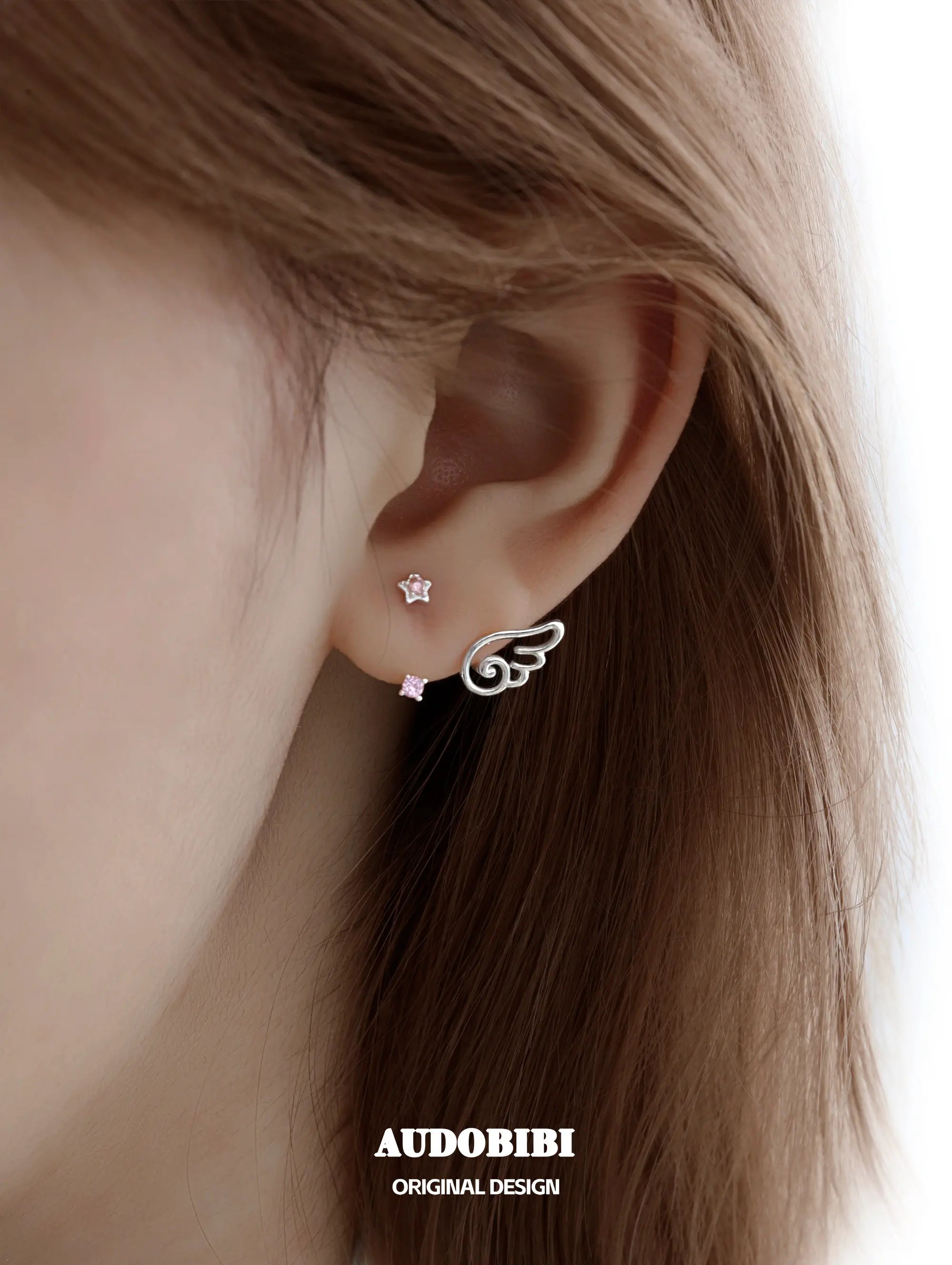 Star-and-wing stud earrings, shown in a close-up of the ear.