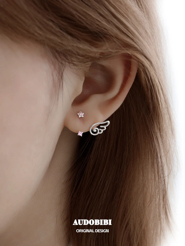 Star-and-wing stud earrings, shown in a close-up of the ear.