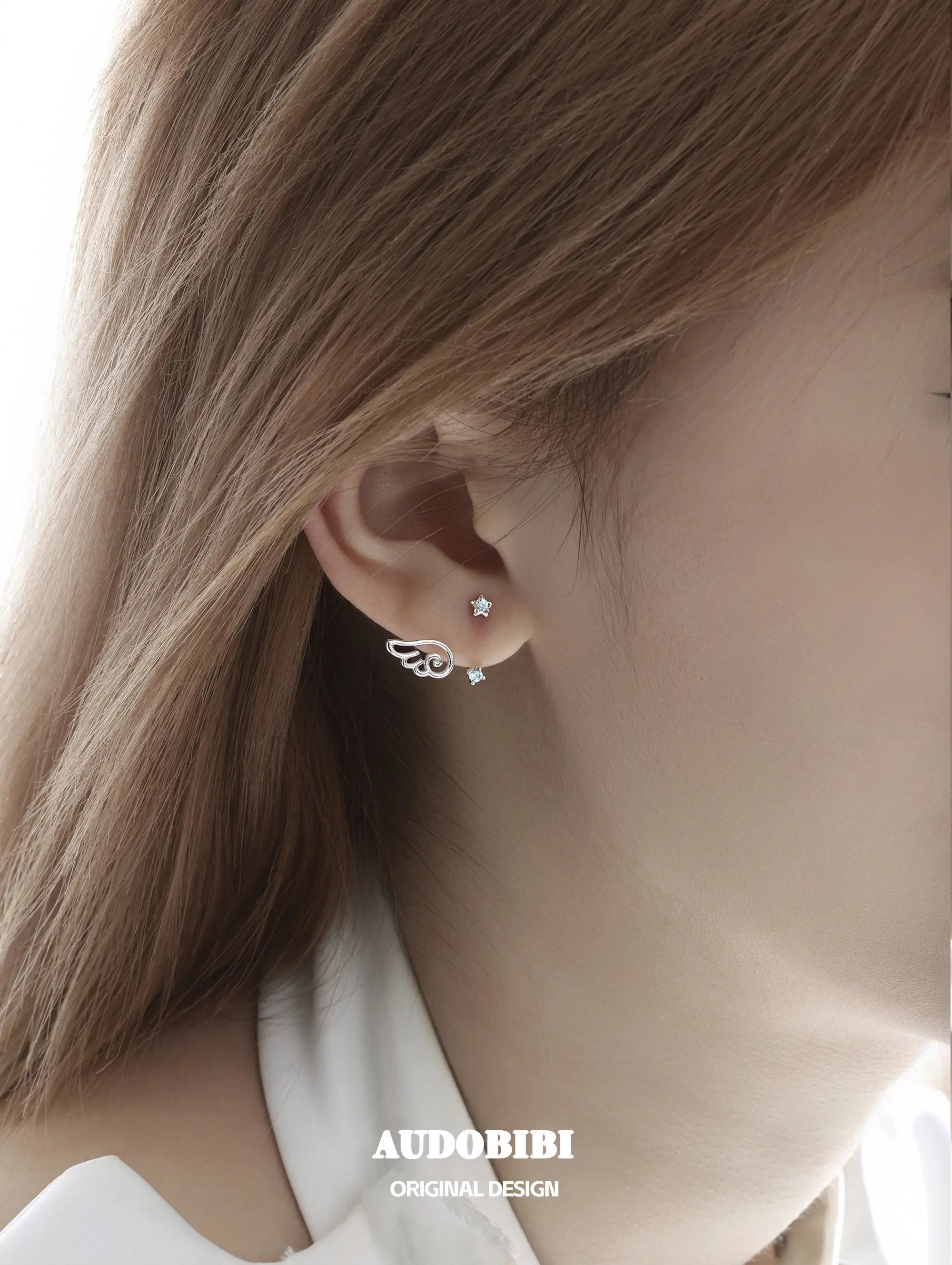Star-and-wing stud earrings, shown in a close-up of the ear.