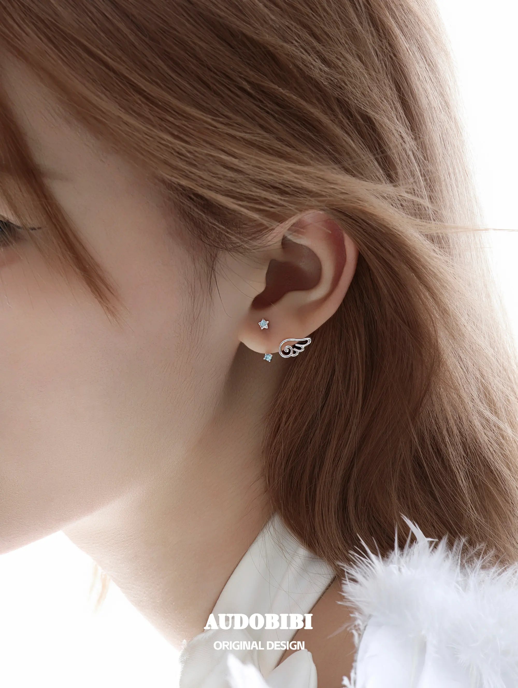 Star-and-wing stud earrings, shown in a close-up of the ear.