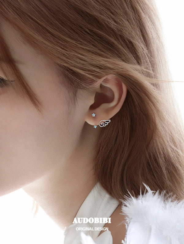 Star-and-wing stud earrings, shown in a close-up of the ear.
