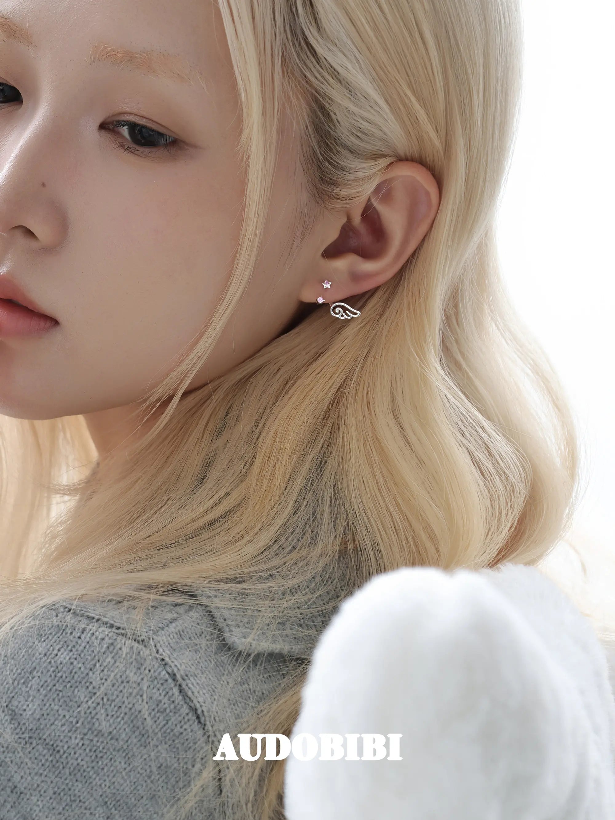 Star-and-wing stud earrings, worn with other jewelry in a model portrait.