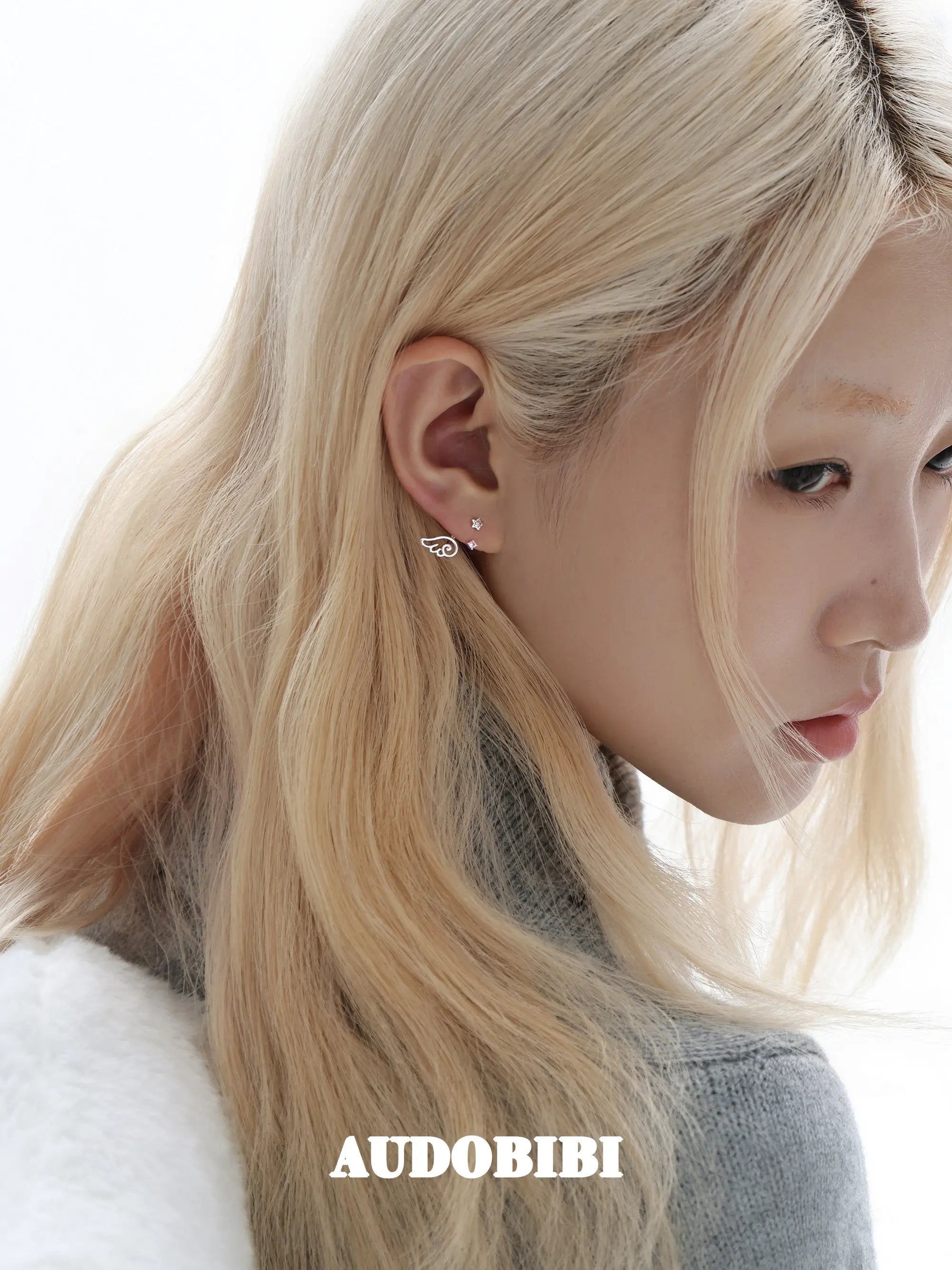 Star-and-wing stud earrings, worn with other jewelry in a model portrait.