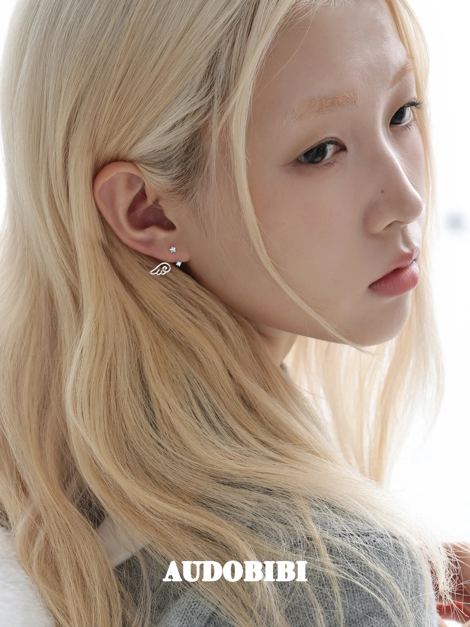 Star-and-wing stud earrings, worn with other jewelry in a model portrait.