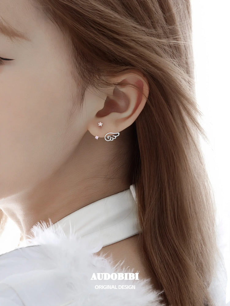 Star-and-wing stud earrings, shown in a close-up of the ear.