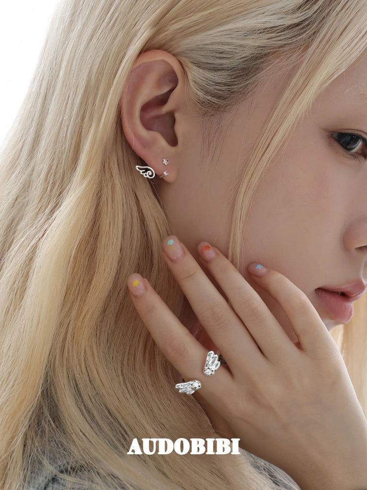 Open ring with rounded angel wings, worn with other jewelry in a model portrait.