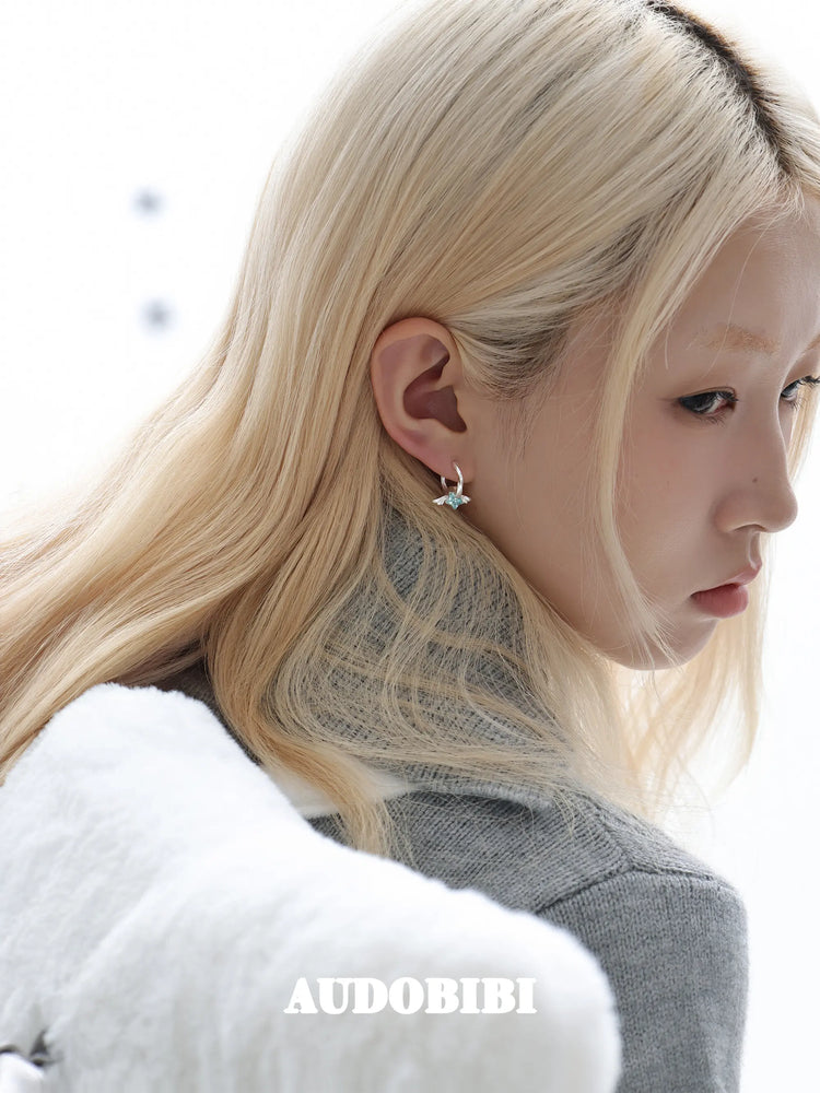 Mini wing-and-star hoop earrings, worn with other jewelry in a model portrait.