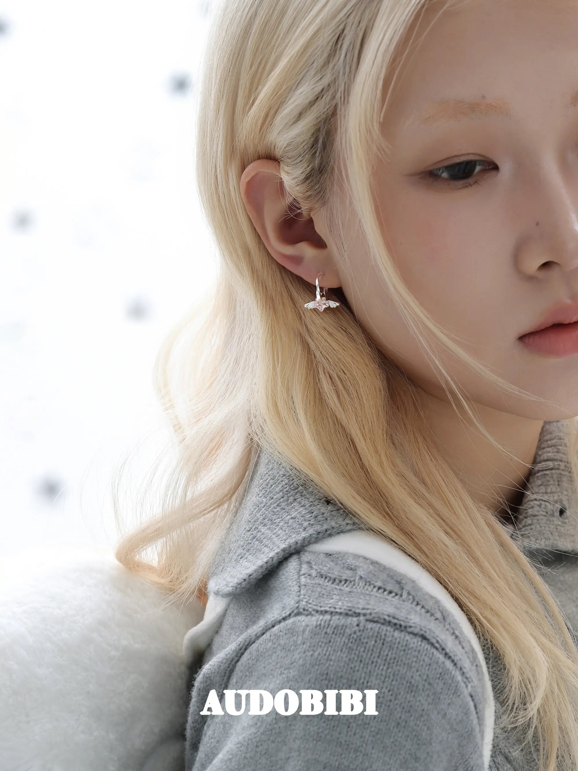 Mini wing-and-star hoop earrings, worn with other jewelry in a model portrait.