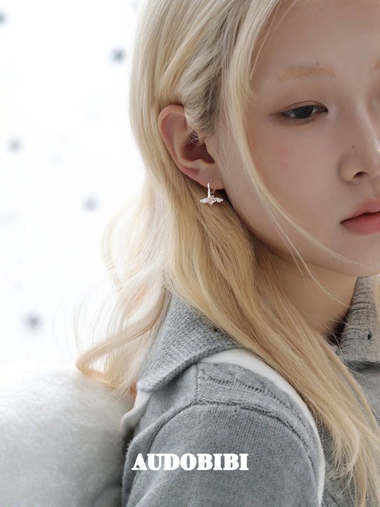 Mini wing-and-star hoop earrings, worn with other jewelry in a model portrait.