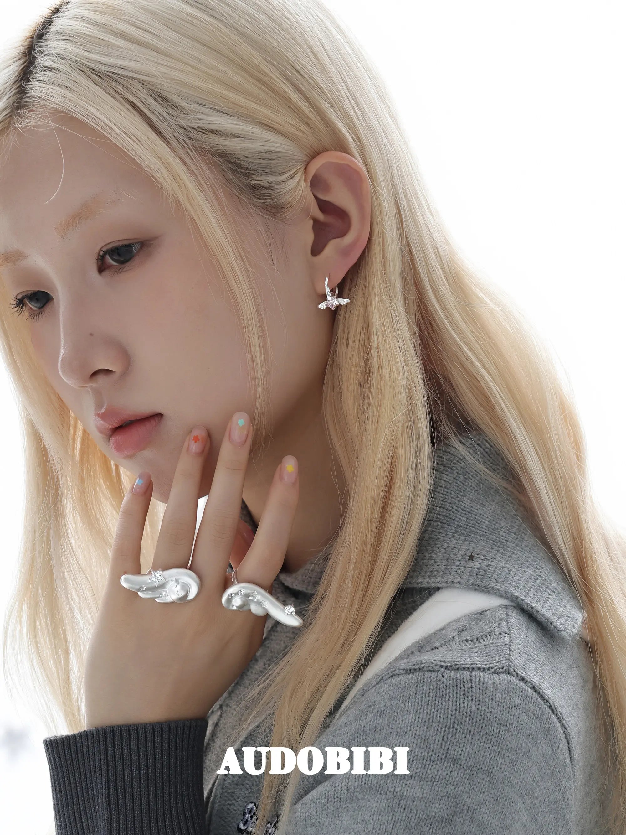 Mini wing-and-star hoop earrings, worn with other jewelry in a model portrait.