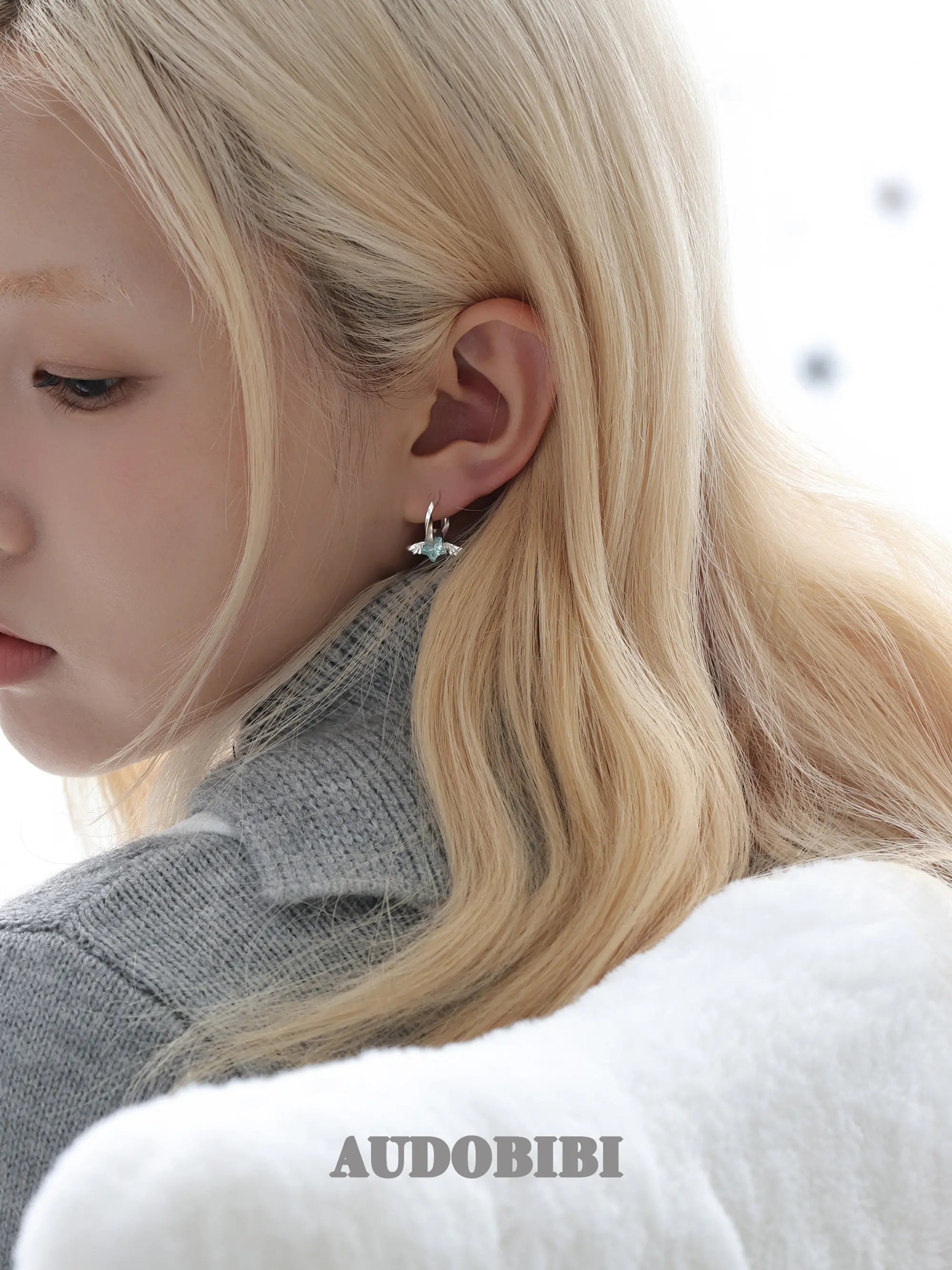 Mini wing-and-star hoop earrings, shown in a close-up of the ear.