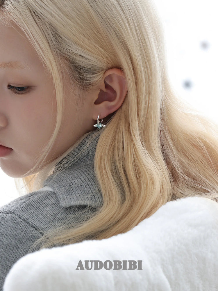 Mini wing-and-star hoop earrings, shown in a close-up of the ear.