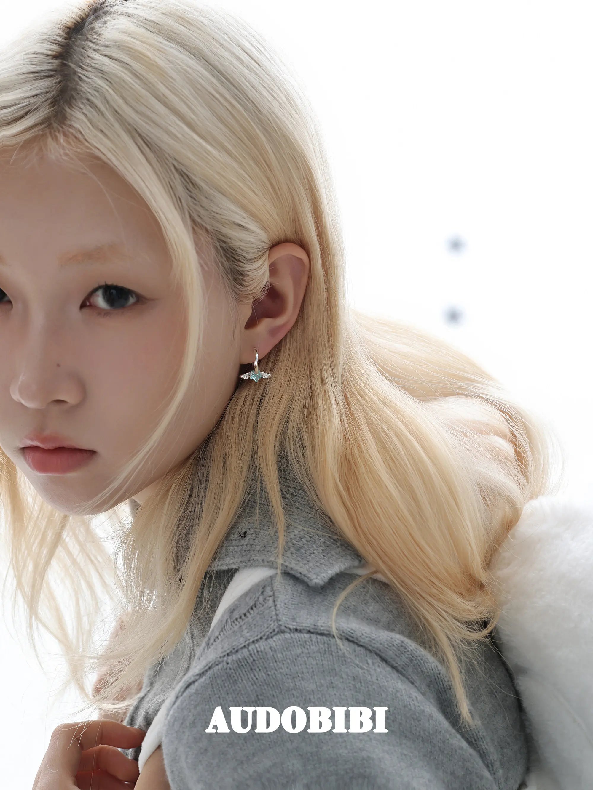 Mini wing-and-star hoop earrings, worn with other jewelry in a model portrait.