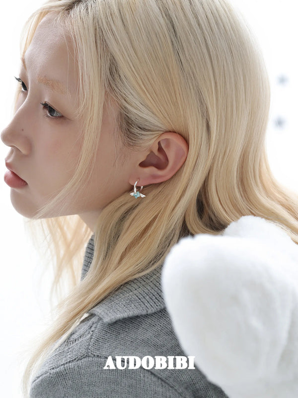 Mini wing-and-star hoop earrings, worn with other jewelry in a model portrait.
