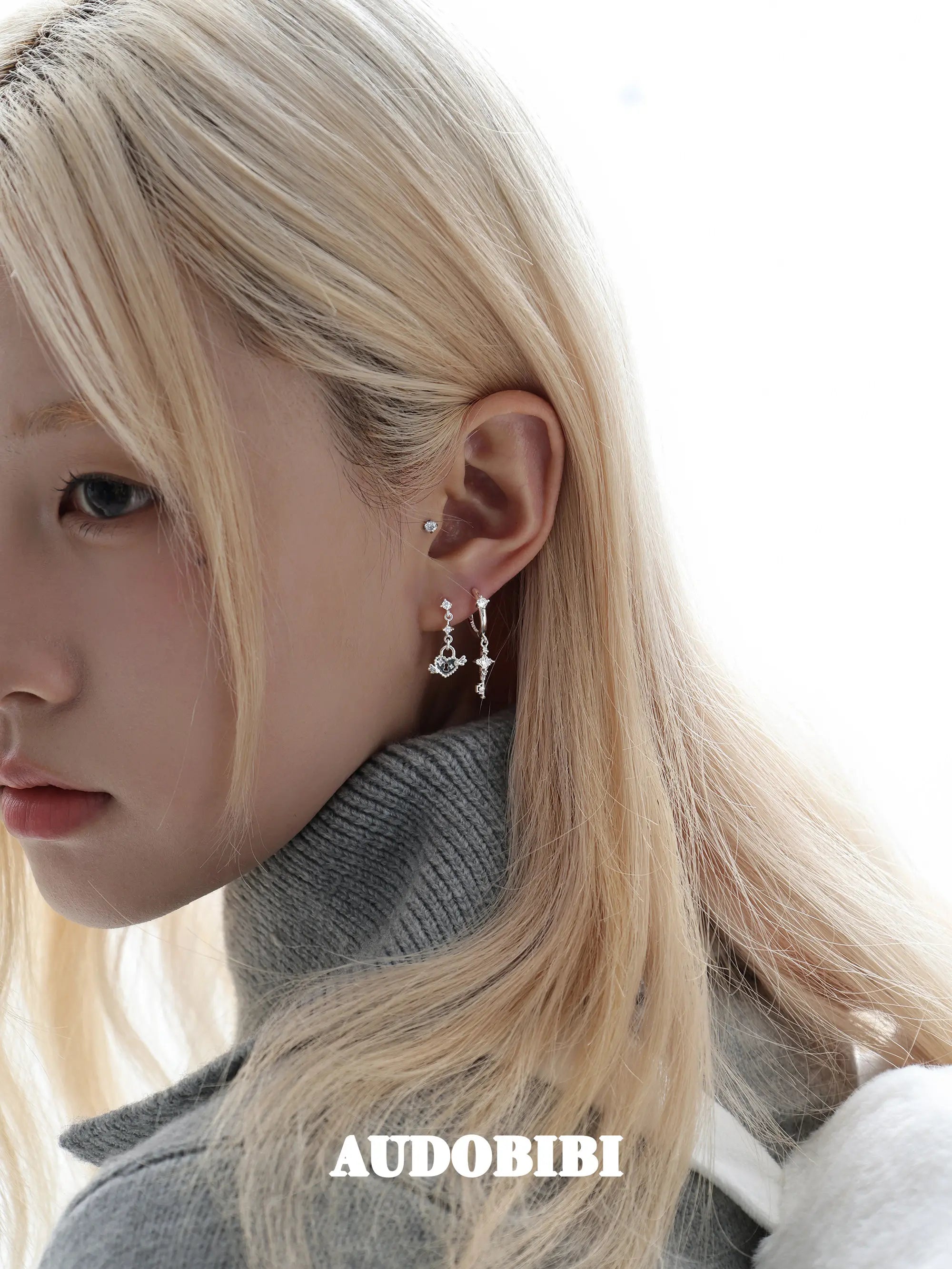 Key and heart-lock earrings, worn with other jewelry in a model portrait.