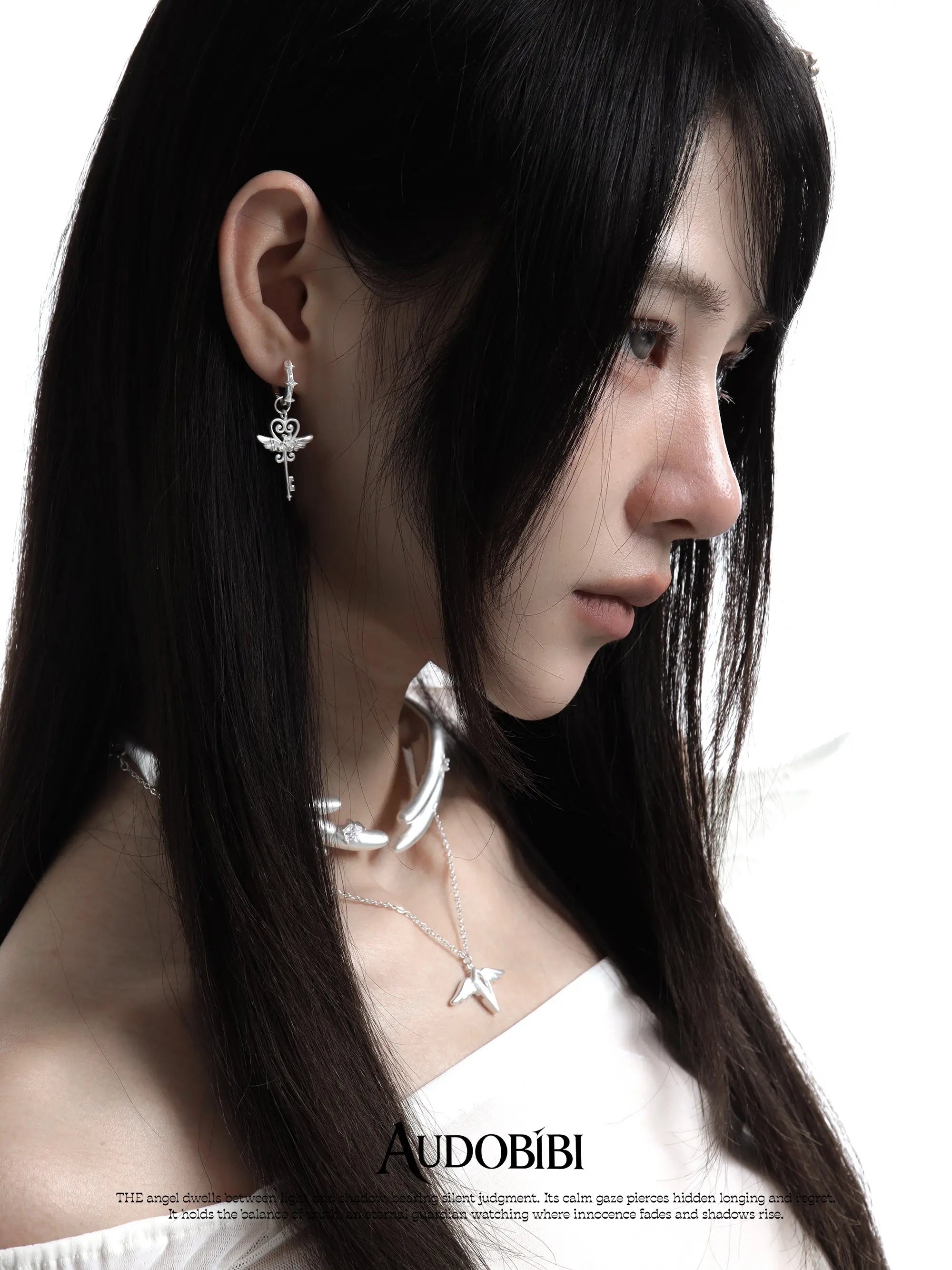 Winged-key hoop earrings, worn with other jewelry in a model portrait.