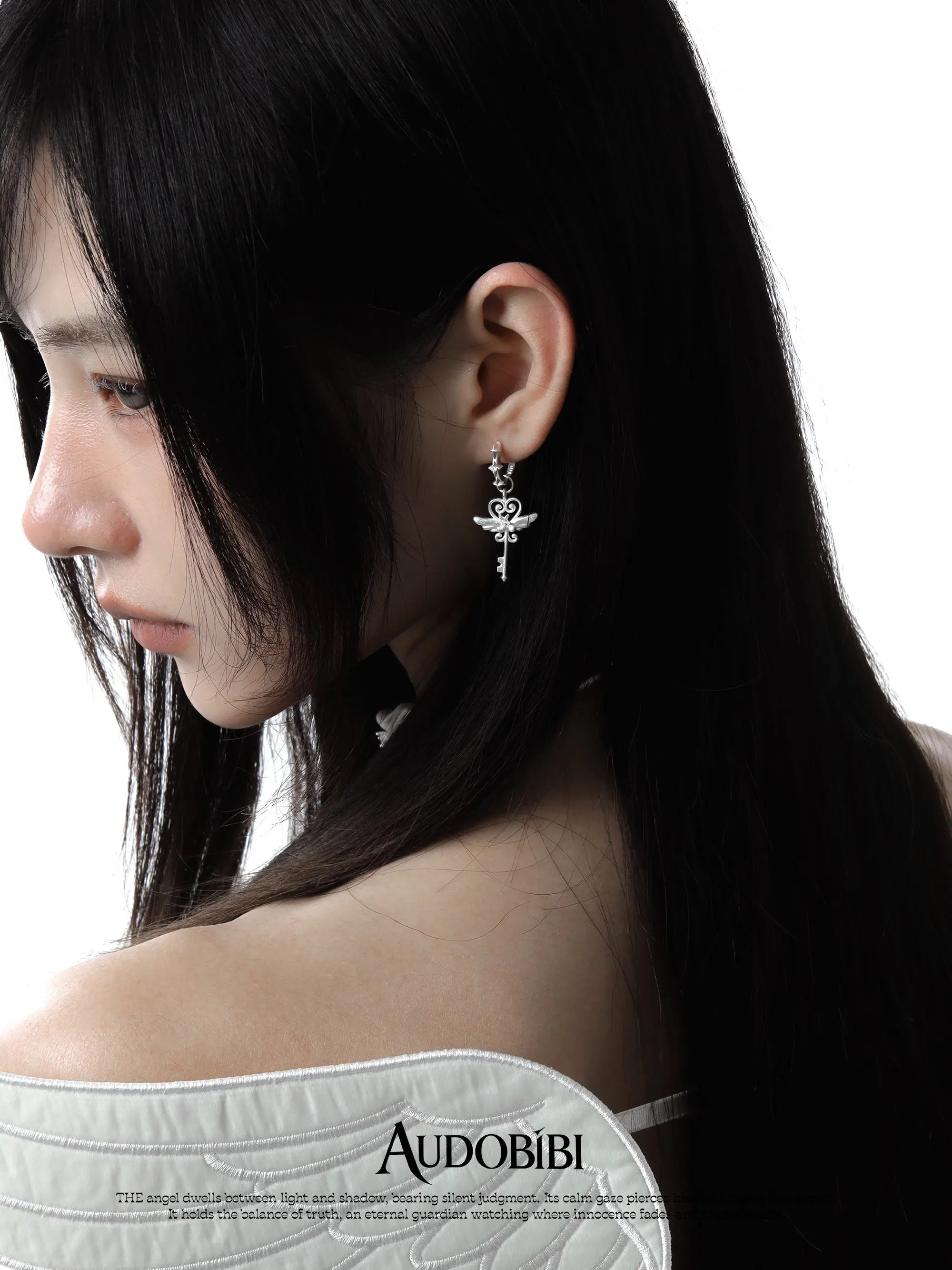 Winged-key hoop earrings, worn with other jewelry in a model portrait.