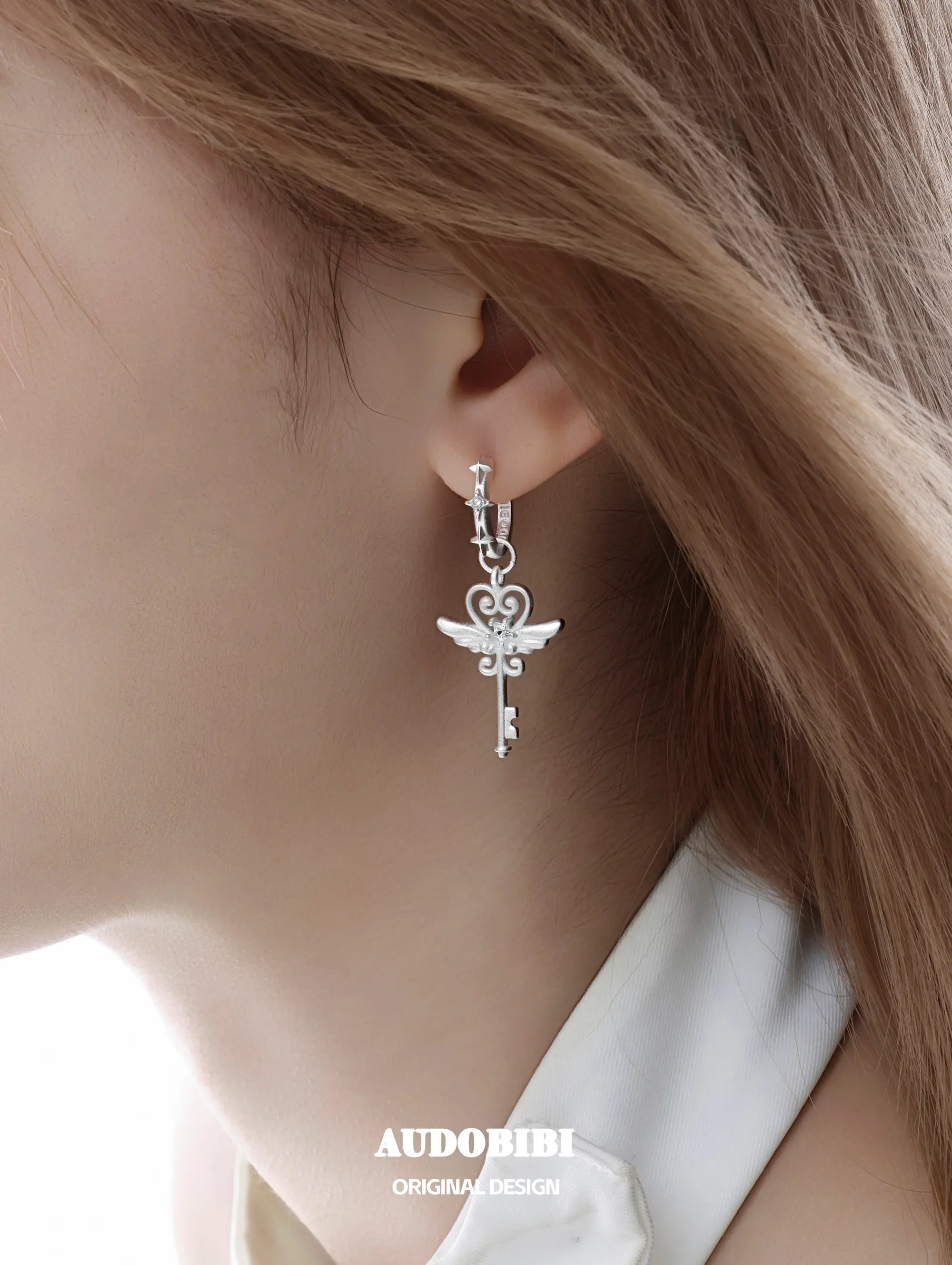 Winged-key hoop earrings, shown in a close-up of the ear.