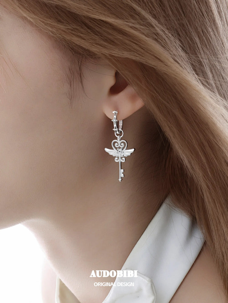 Winged-key hoop earrings, shown in a close-up of the ear.