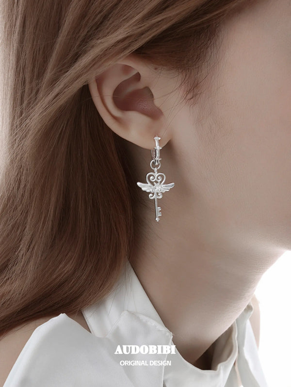Winged-key hoop earrings, shown in a close-up of the ear.
