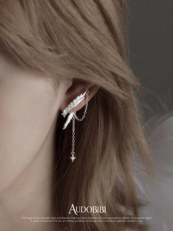 Asymmetric wing earrings with chain drops, shown in a close-up of the ear.