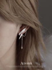 Asymmetric wing earrings with chain drops, shown in a close-up of the ear.