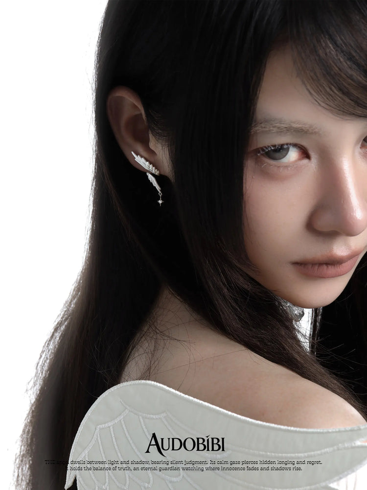 Asymmetric wing earrings with chain drops, worn with other jewelry in a model portrait.