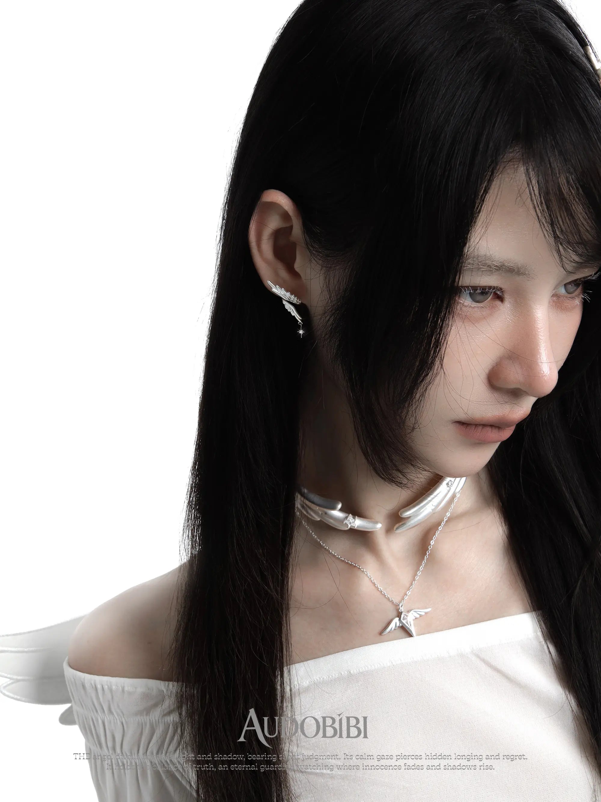 Asymmetric wing earrings with chain drops, worn with other jewelry in a model portrait.